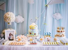 a table topped with lots of cakes and cupcakes next to a wall covered in clouds