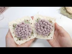 someone is holding two crocheted squares in their hands, one has a flower on it