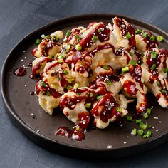 a black plate topped with food covered in sauce and green onions on top of a wooden table