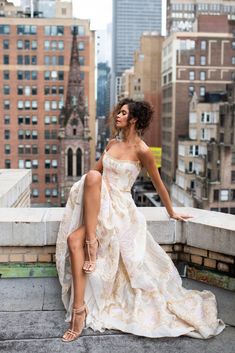 a woman in a white dress is sitting on a ledge and posing for the camera