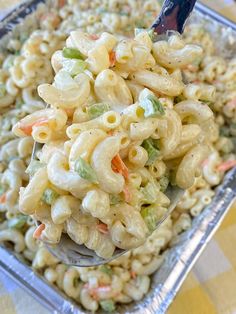 a spoon full of macaroni and cheese salad on a tray with a checkered tablecloth