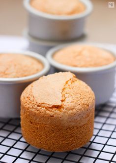 four cupcakes sitting on top of a cooling rack with white cups in the background