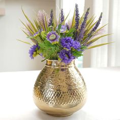 a gold vase filled with purple flowers on top of a table