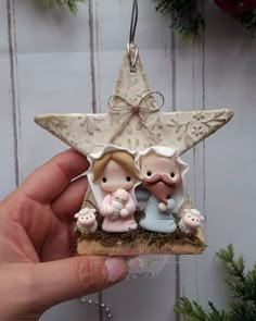 a hand holding a christmas ornament with two small figurines on it