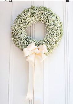 a white wreath with a bow hanging on the front door to hang it's doors