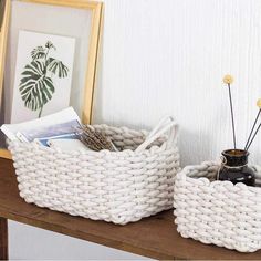 two white baskets sitting on top of a wooden table next to pictures and other items