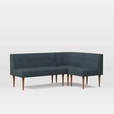 a blue couch with wooden legs sitting on top of a white floor next to a gray wall