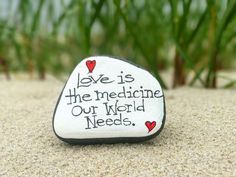 a rock with the words love is the medicine our world needs on it sitting in sand