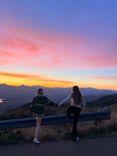 two people holding hands while standing on top of a hill at sunset with mountains in the background