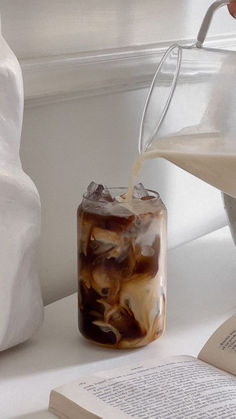 an iced drink being poured into a glass jar on top of a table next to a book