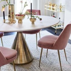 a dining room table with pink velvet chairs and gold vases on the centerpiece