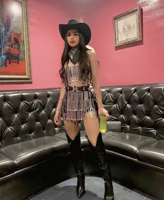 a woman in a short dress and cowboy hat standing next to a black leather couch