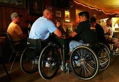 several men sitting at a table with their backs to each other, in wheelchairs