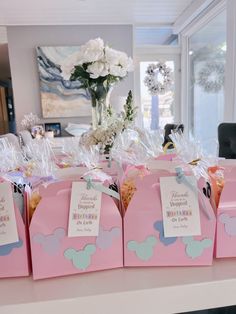 pink bags with mickey mouse tags on them sitting on a table in front of flowers