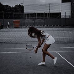 a woman in white dress playing tennis on an asphalt court with dark clouds above her