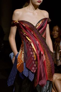 a woman in a dress with many ties on her head and shoulders, walking down the runway