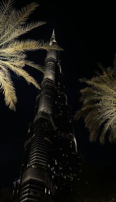 the burj tower is lit up at night with palm trees in front of it