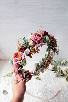 a hand holding a flower crown on top of a white surface with pink and green flowers