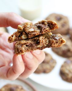 a person holding up some cookies with chocolate chips on them and milk in the background