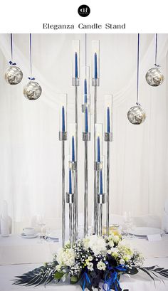 a centerpiece with blue candles and flowers on a white table cloth, surrounded by hanging glass balls