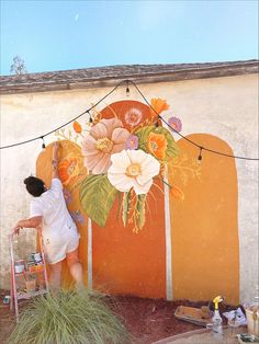 a man is painting a mural on the side of a building with flowers and leaves