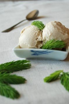 two scoops of ice cream in a bowl with green leaves on the table next to utensils