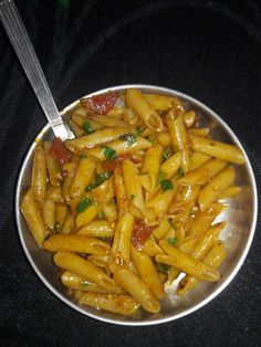 a silver bowl filled with pasta on top of a black countertop next to a fork