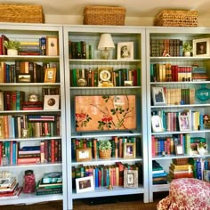 a room filled with lots of books on top of white bookcases next to a chair