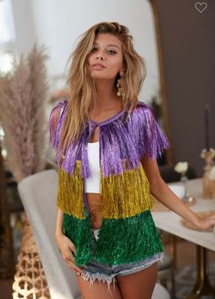 a woman standing in front of a table wearing a purple and green fringed jacket