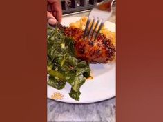 a person is holding a fork over some food on a plate with greens and potatoes