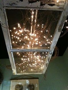 an open window with lights in it and the caption reads, old screen door hanging from ceiling with lights and branches - how clever is this perfect for patio or outdoor event?