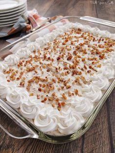 a glass dish filled with white frosting and toppings on top of a wooden table