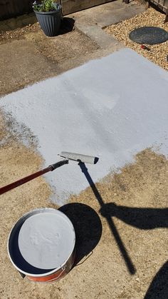 a bucket and paint roller on the ground in front of a backyard area with gravel