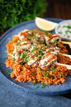 a blue plate topped with chicken and rice next to lemon wedges on a wooden table