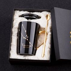 a black coffee cup and spoon in a box with gold lettering on the lid that says taurus