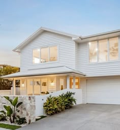 a white two story house with large windows and plants in the front yard at dusk