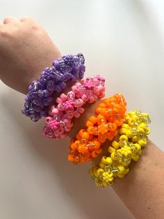 four different colored bracelets on someone's arm, one is made out of plastic beads