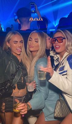 three women are posing for the camera in front of a crowd at a nightclub with drinks