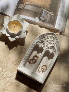 a candle holder with two rings on it next to an open book and a flower