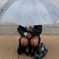 a woman sitting on the ground with an umbrella over her head, holding a purse