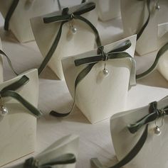 many small white boxes with green ribbons tied around the edges and pearls on them, sitting on a table