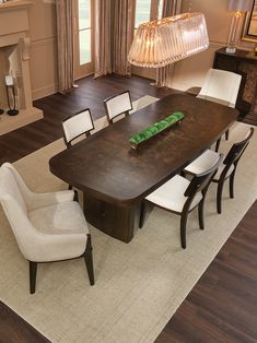 a dining room table with chairs and a vase on the center piece, in front of a fireplace