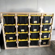 several black and yellow plastic containers are stacked on wooden shelves in a storage room with white walls