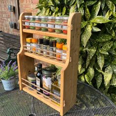 a wooden spice rack sitting on top of a metal table next to a green bush