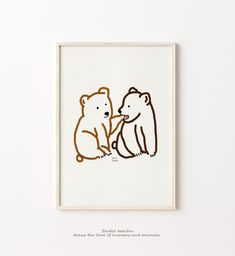 two brown bears sitting next to each other on a white surface in front of a framed wall