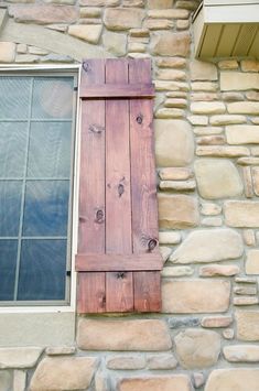 an open window on the side of a stone building with wooden shutters and wood slats