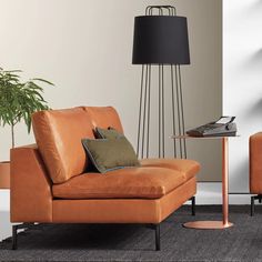 a living room with an orange couch and black floor lamp next to a table that has a laptop on it