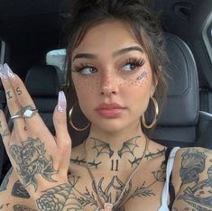 a woman with tattoos on her chest holding up two fingers and wearing large hoop earrings