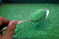 a spoon with green sugar on it is being held by a person's hand