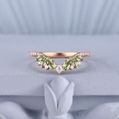 a gold ring with green leaves and white diamonds on the top, sitting on a table